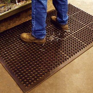 operario de pie sobre alfombra antifatiga perforada para uso industrial